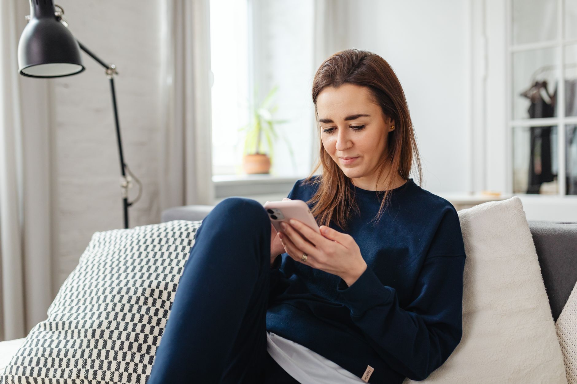 a woman sitting alone on a couch looking at her phone with a concerned expression