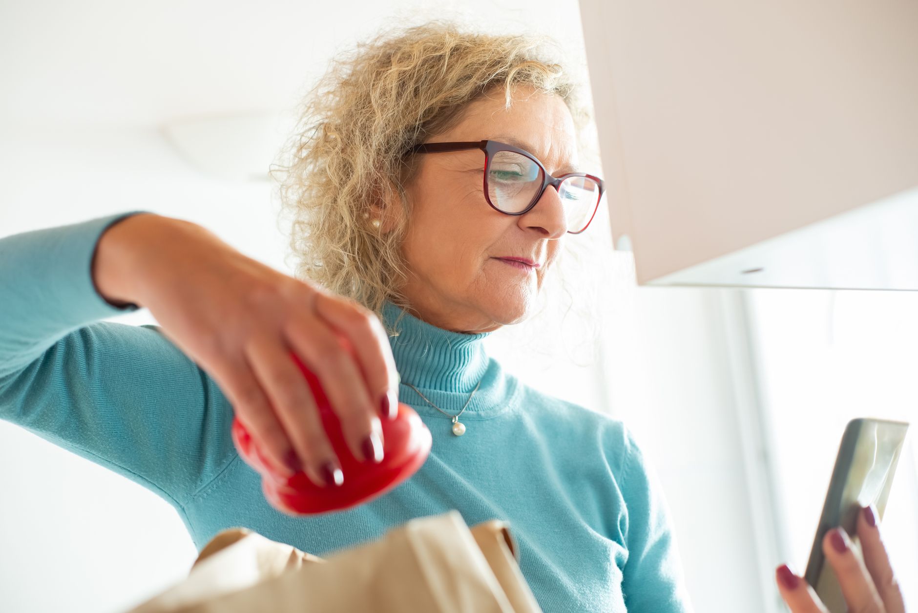 A senior woman with a worried expression holding a smartphone while sitting at a kitchen table